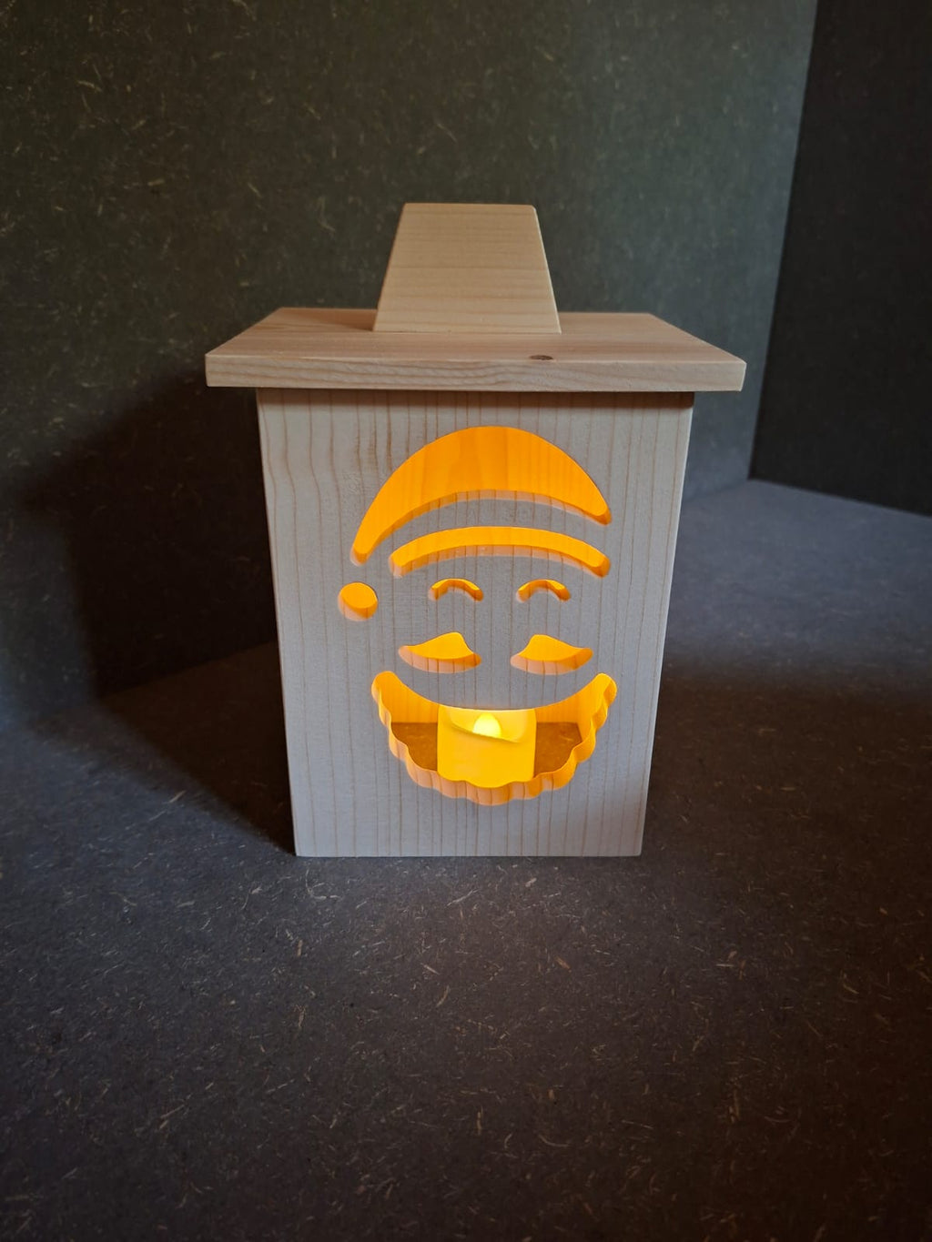 Drei handgefertigte LED-Weihnachtslaternen aus hellem Holz mit ausgesägten Motiven Weihnachtsmann, Tannenbaum und Kerze.