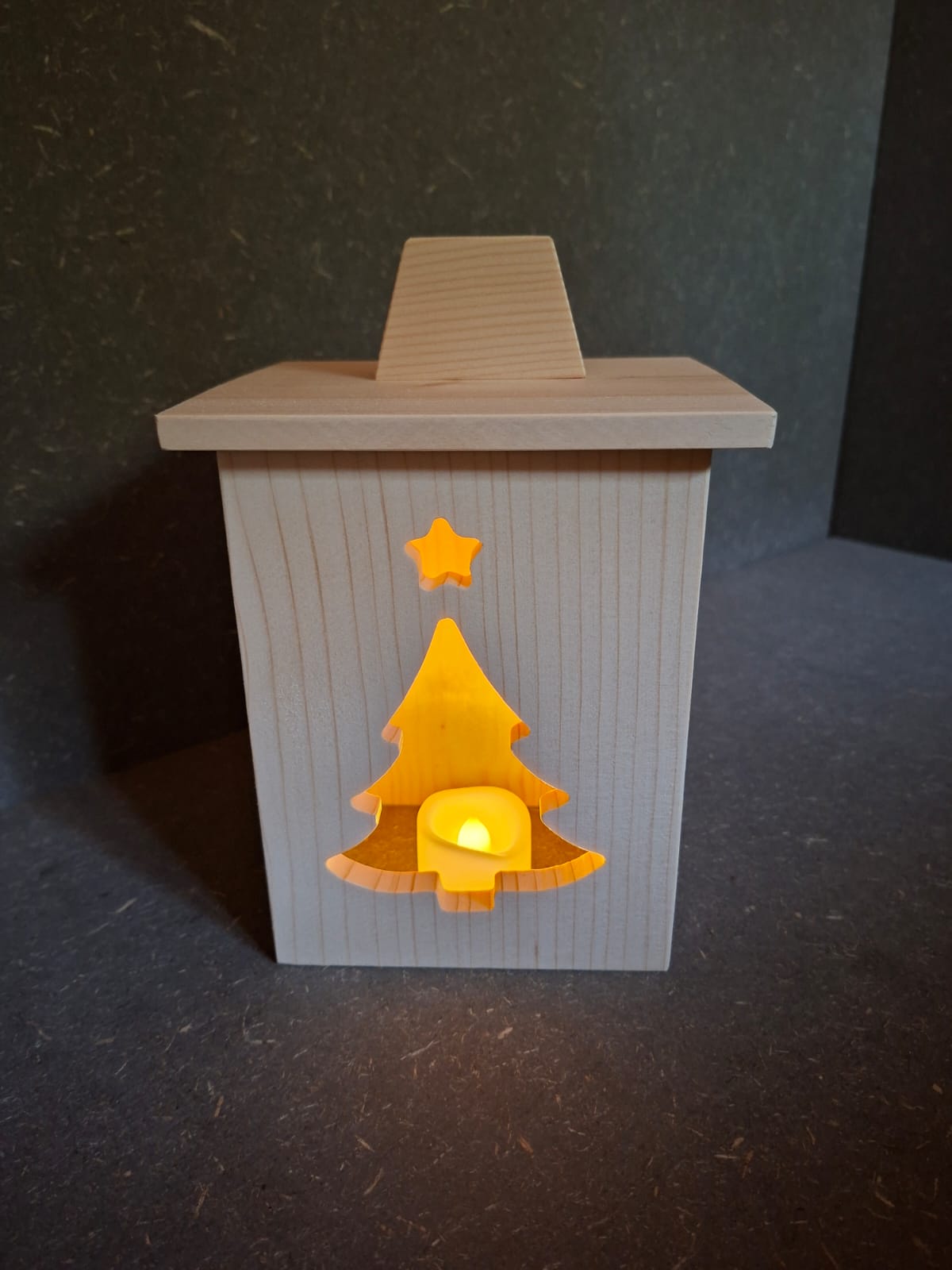 Drei handgefertigte LED-Weihnachtslaternen aus hellem Holz mit ausgesägten Motiven Weihnachtsmann, Tannenbaum und Kerze. Tannenbaum beleuchtet.
