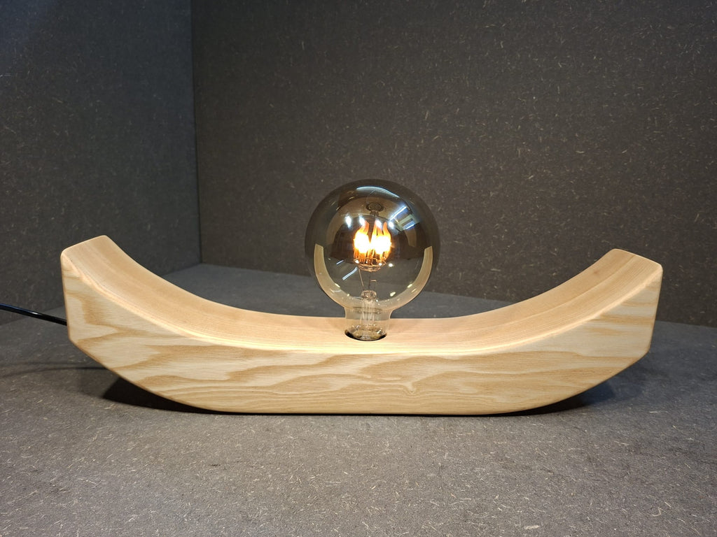 Handgefertigte Holzlampe Lichtbogen aus geöltem Eschenholz mit geschwungenem Sockel und leuchtender Glaskugel mit flackerndem Licht.