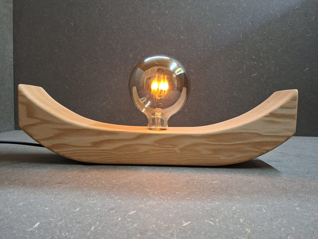 Handgefertigte Holzlampe Lichtbogen aus geöltem Eschenholz mit geschwungenem Sockel und leuchtender Glaskugel mit flackerndem Licht.