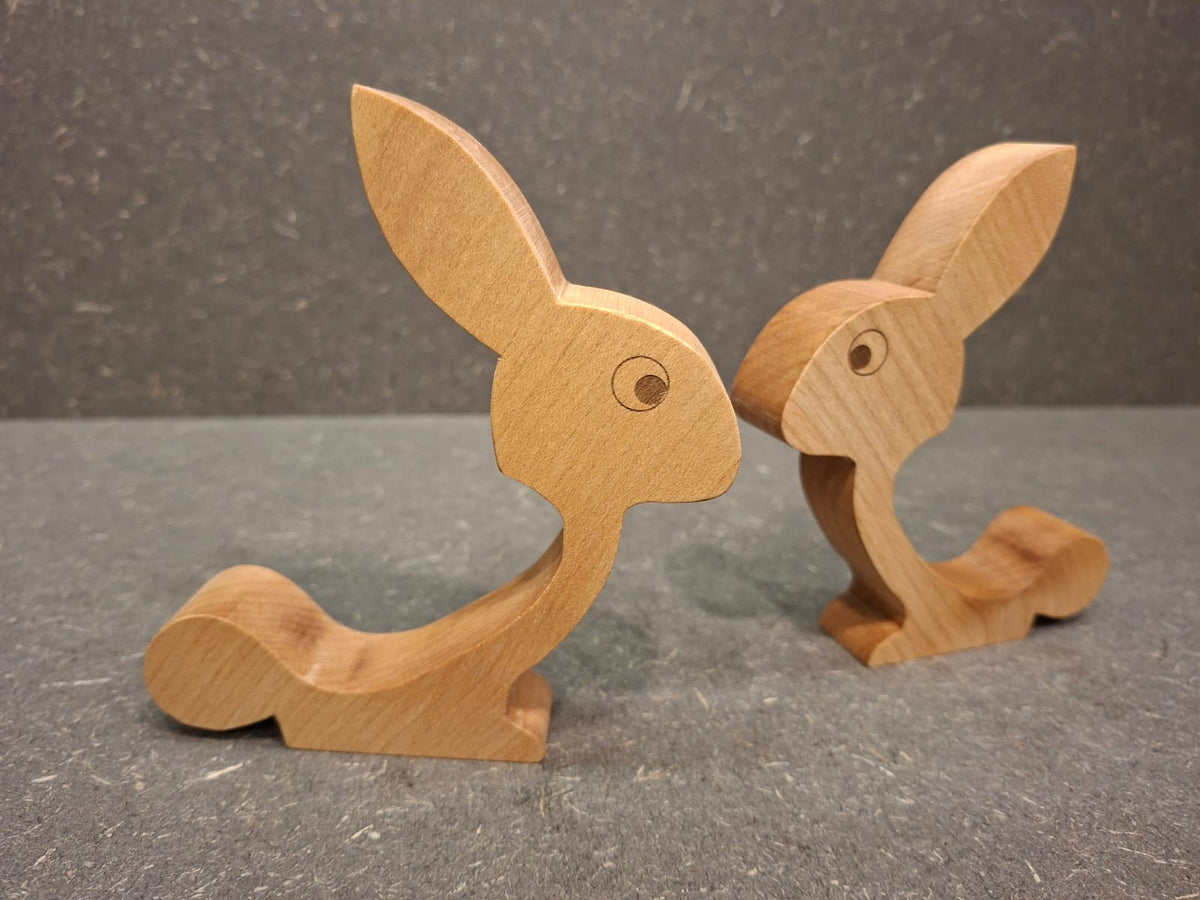 Handgefertigter Eierhalter aus geöltem Ahorn in Hasenform mit Ei auf dem Rücken als Osterdekoration.