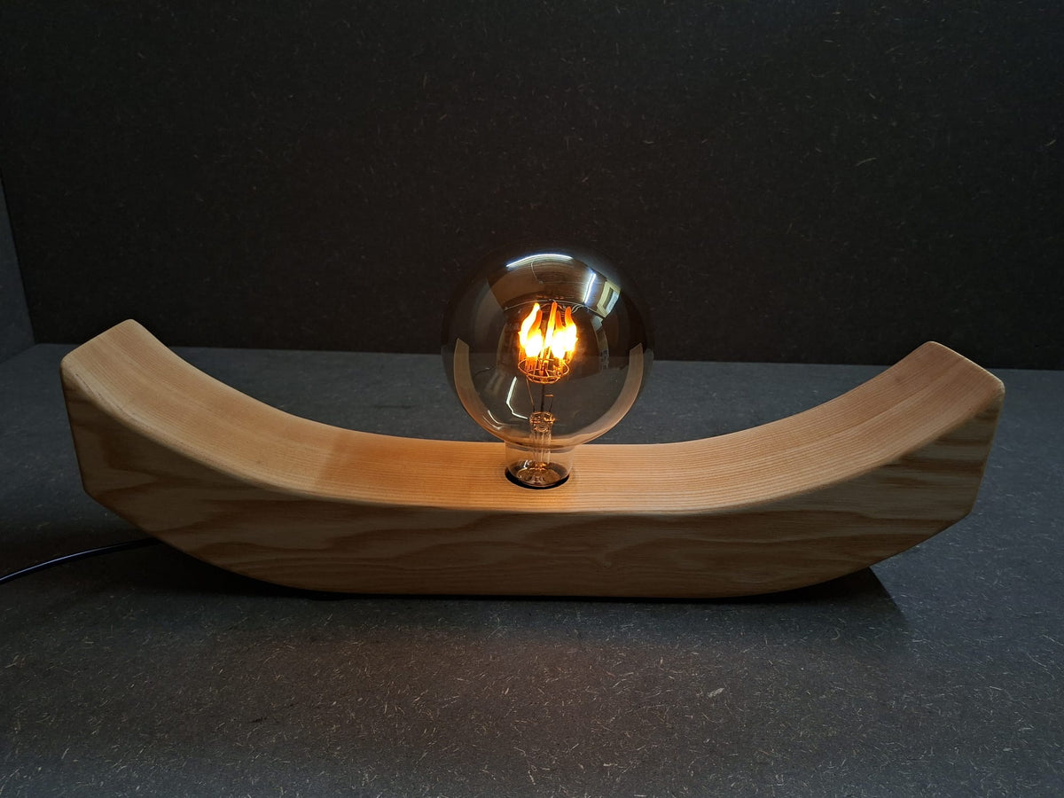 Handgefertigte Holzlampe Lichtbogen aus geöltem Eschenholz mit geschwungenem Sockel und leuchtender Glaskugel mit flackerndem Licht.