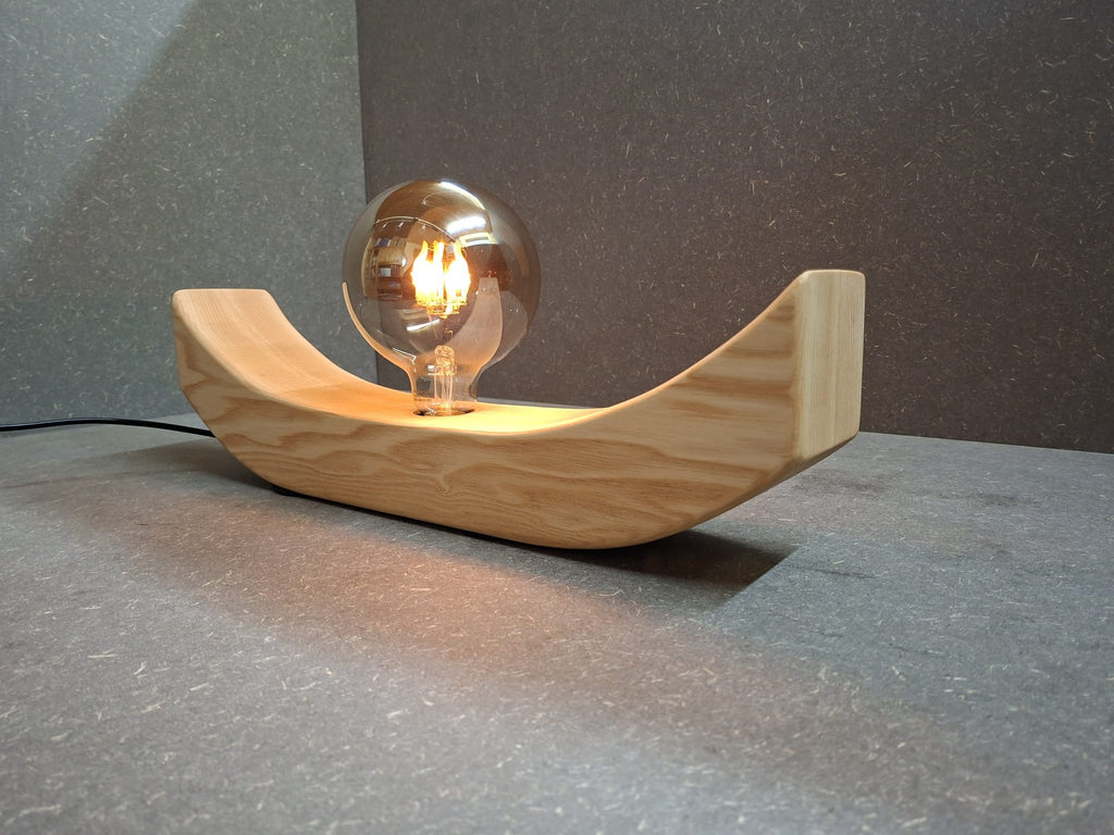 Handgefertigte Holzlampe Lichtbogen aus geöltem Eschenholz mit geschwungenem Sockel und leuchtender Glaskugel mit flackerndem Licht.