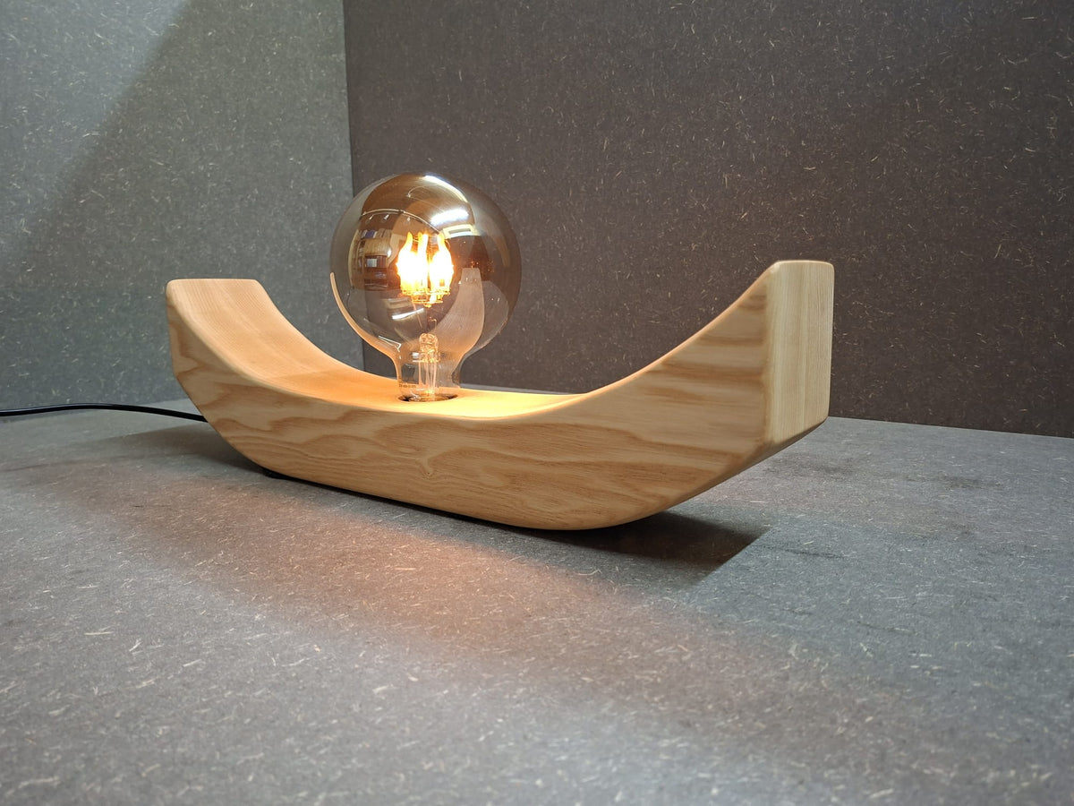 Handgefertigte Holzlampe Lichtbogen aus geöltem Eschenholz mit geschwungenem Sockel und leuchtender Glaskugel mit flackerndem Licht.