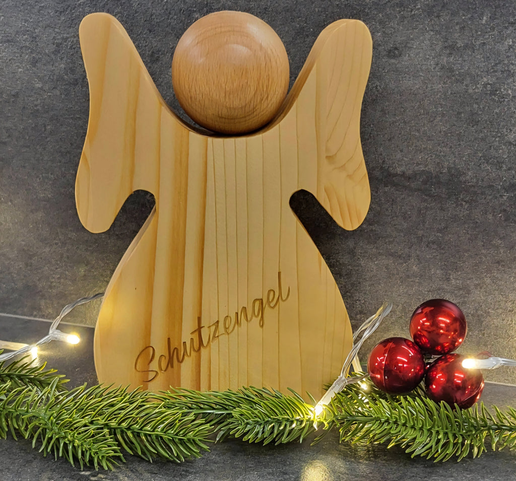 Handgefertigter Schutzengel aus Holz mit individueller Gravur als persönliches Geschenk.
Engel mit Gravur: Schutzengel 
Auf dem Bild sind noch Tannenzweige, Lichterkette und rote Kugeln. Der Engel ist auch ein tolles Weihnachtsgeschenk 