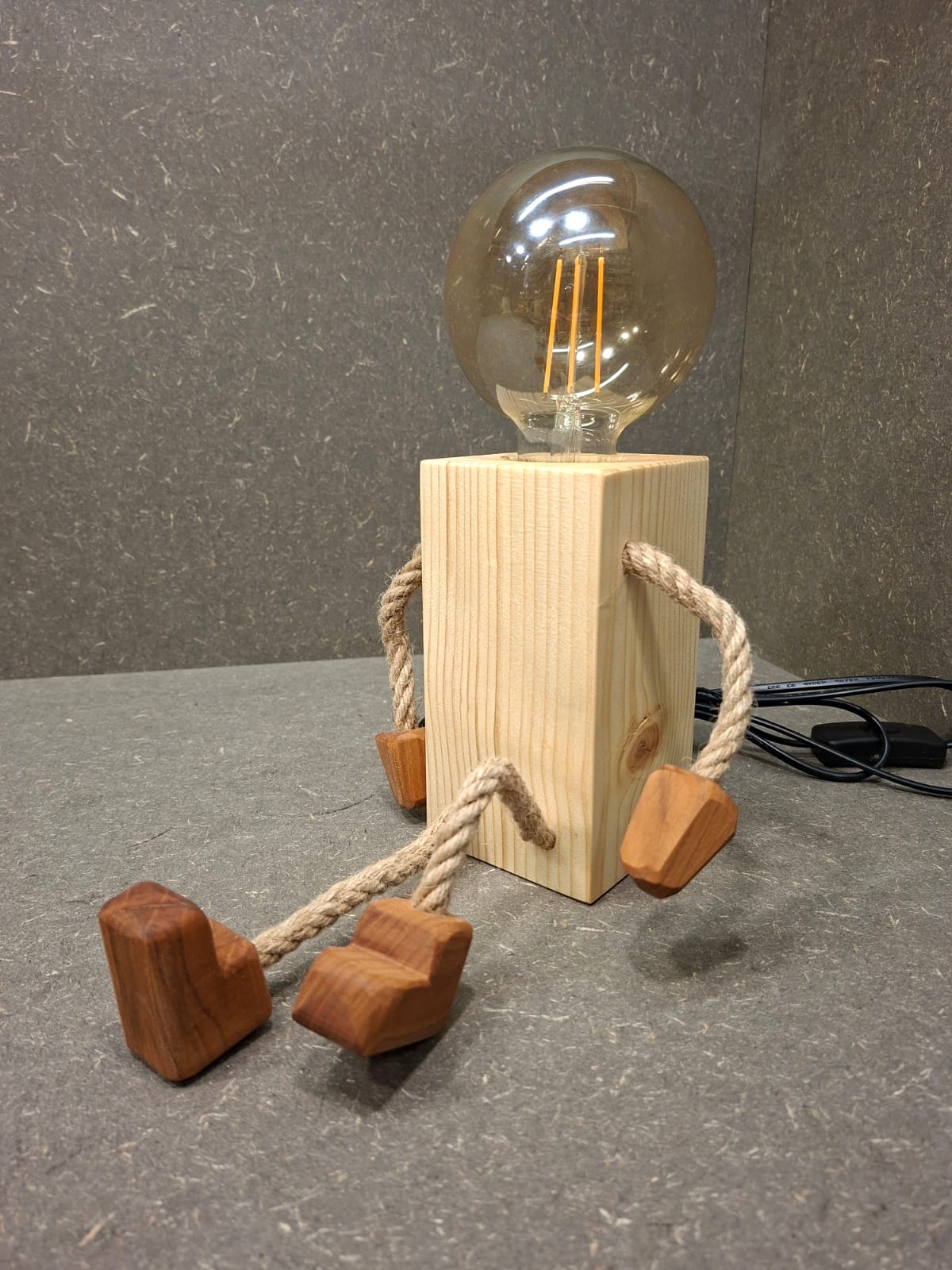 Handgefertigtes Lampen Männchen aus Fichte und Kirschholz mit beweglichen Seilarmen und -beinen als Tischlampe und Kantenhocker.