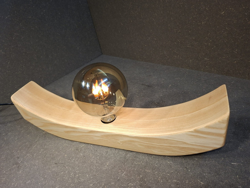 Handgefertigte Holzlampe Lichtbogen aus geöltem Eschenholz mit geschwungenem Sockel und leuchtender Glaskugel mit flackerndem Licht.