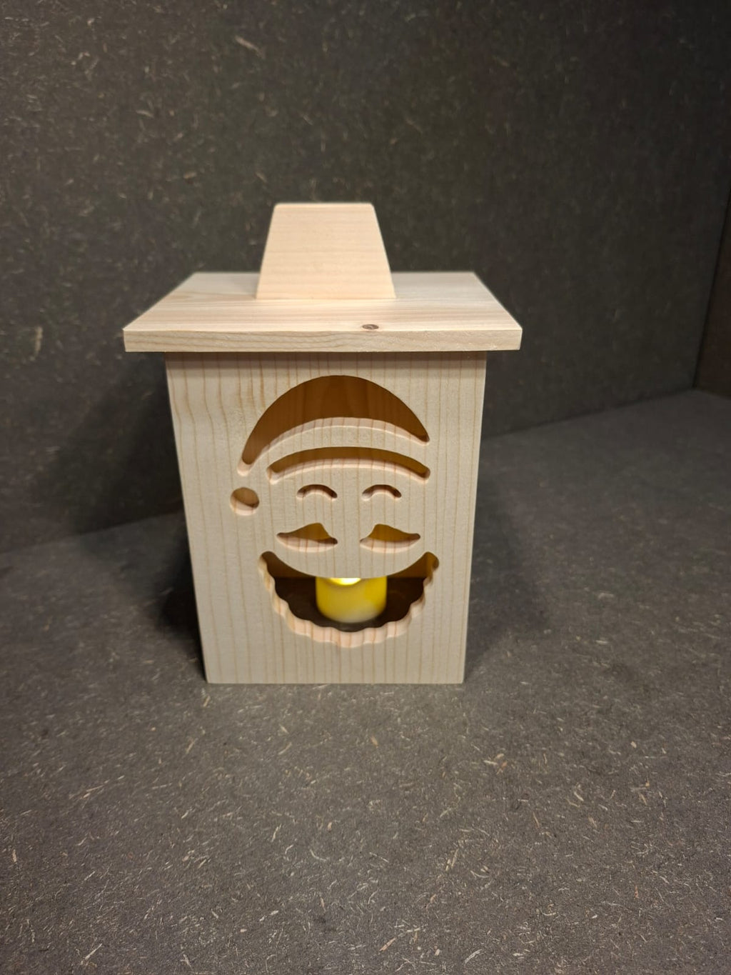 Drei handgefertigte LED-Weihnachtslaternen aus hellem Holz mit ausgesägten Motiven Weihnachtsmann, Tannenbaum und Kerze.